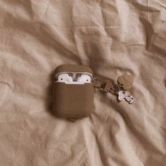 an airpods case sitting on top of a bed next to two keychains