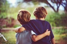 two young boys hugging each other in the woods