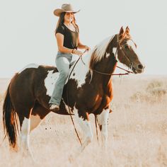 a woman riding on the back of a brown and white horse in an open field