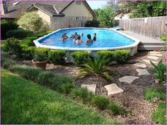 several people are in the pool surrounded by plants and rocks, near a fenced backyard