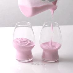 a person pouring pink liquid into two wine glasses