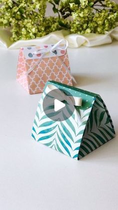 two small boxes sitting next to each other on a white table with flowers in the background