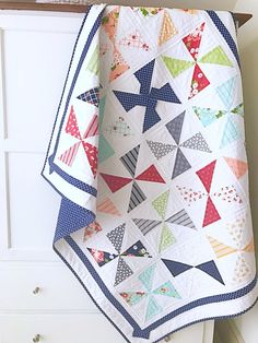 a colorful quilt hanging on the side of a white dresser next to a wooden shelf