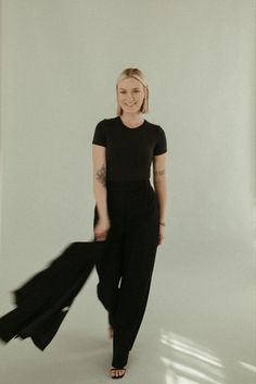 a woman standing in front of a white wall wearing black pants and a t - shirt