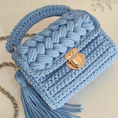 a blue crocheted purse with a gold handle and tasselled chain attached to it