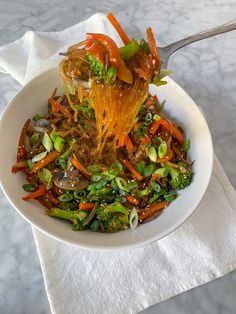 a white bowl filled with vegetables on top of a table next to a napkin and fork