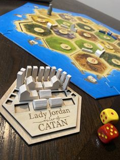 a wooden board game with dices sitting on the table next to it and lady jordan's catan