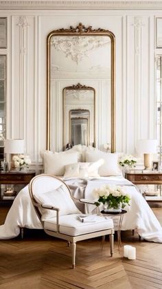 an elegant bedroom with white furniture and gold mirrors on the wall, along with wooden flooring