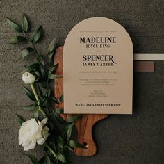 a wooden cutting board with flowers on it and a wedding card attached to the back