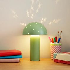 a green lamp sitting on top of a wooden table next to books and pencils