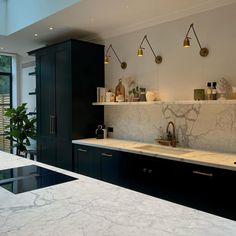 a kitchen with marble counter tops and black cabinets, along with hanging lights above the sink