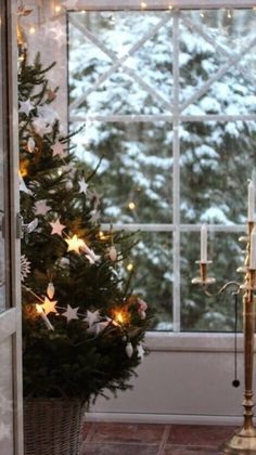 a small christmas tree sitting in front of a window next to a candelabra