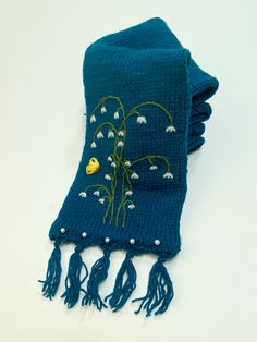 a blue scarf with white flowers and tassels on the end, sitting on a table