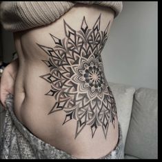 a woman's stomach with a tattoo design on the side of her belly and an intricate flower