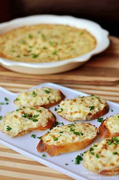 several small pieces of bread with cheese and herbs on them next to a casserole dish