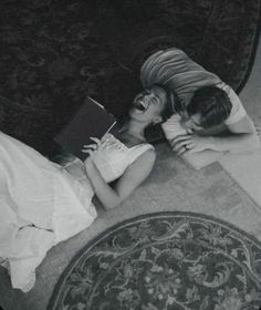 two people are laying on the floor with a book in their hands and looking at each other