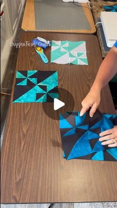 someone is cutting out blue and white paper squares on a wooden table with scissors, tape and glue