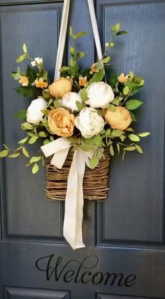 a welcome sign hanging on the front door with flowers in a basket attached to it