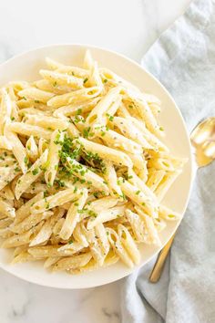 a white bowl filled with pasta and parsley on top of a marble countertop