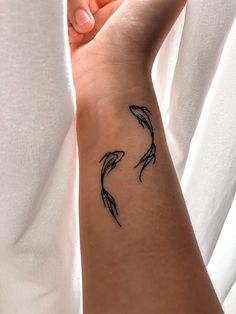 a woman's arm with two black fish tattoos on it