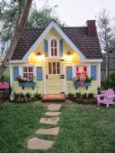 a small yellow house with blue shutters and flowers on the window sill is lit up