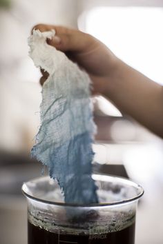 a person holding something in their hand over a cup filled with liquid and tissue paper