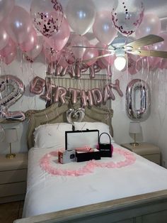 a bed with pink and white balloons on the headboard, along with a birthday cake