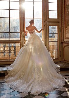 a woman in a wedding dress is standing by a window with the sun shining on her