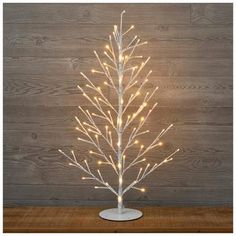 a white christmas tree with lights on it in front of a wooden wall and floor