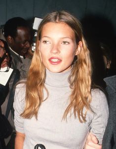 a woman with long blonde hair standing in front of a group of people at an event