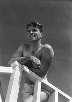 a man sitting on top of a white chair next to a wooden railing and holding his arms crossed