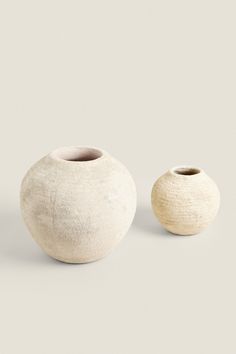 two white vases sitting next to each other on a gray surface with no one around them