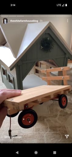 a hand holding a wooden toy truck with a house in the back and red wheels