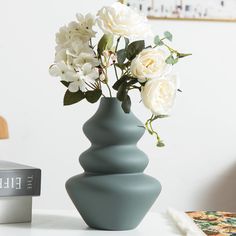 a vase with white flowers sitting on a table next to a stack of books and magazines