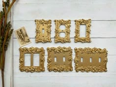 four gold frames are arranged on a white wooden wall with dried flowers and other items