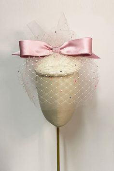 Bunty is a truly beautiful piece of millinery, created in collaboration with Suzannah London and Awon Golding.A playful special occasion button hat which features an ivory buntal button base, adorned with pale pink tulle and crystallised veiling. A charming pink crepe-back satin bow sits proudly atop the hat, framed with frothy veiling and tulle.This feather-light hat attaches with an elastic at the nape of the neck and comb to anchor in the hair.This hat can also be dyed-to-match at our London Luxury Formal Hat With Bow, Luxury Pink Wedding Hat, Pink Wedding Hat With Structured Crown, Elegant Pink Hat With Bow, Pink Adjustable Ribbon Hat, Suzannah London, Hat With Bow, London Boutique, Gown Suit