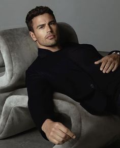 a man sitting on top of a gray couch next to a white chair and looking at the camera