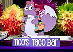 a purple table topped with lots of colorful flowers and paper cut outs that say taco's taco bar