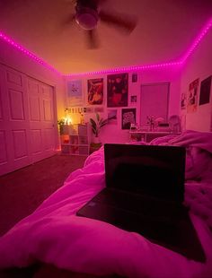 a laptop computer sitting on top of a bed in a room with pink lights around it