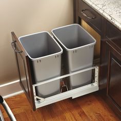 two grey trash cans sitting on top of a wooden floor next to a countertop