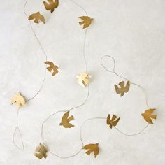 some gold leaves are hanging from a string on a white wall and there is no one in the photo