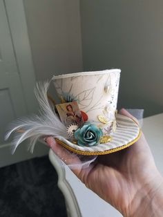 a person is holding a small hat with feathers on the top and a flower in the center