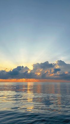 the sun is setting over the ocean with clouds in the sky and water below it