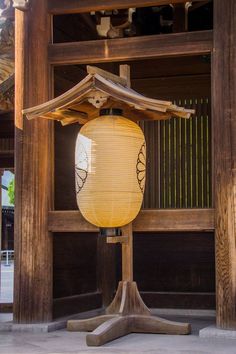 a yellow lantern sitting on top of a wooden stand in front of a building with wood pillars