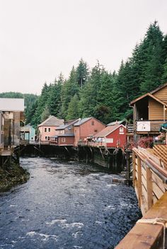 a river running through a small town surrounded by forest covered hills and tall pine trees