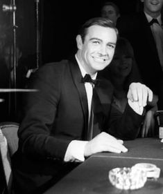 a man in a suit sitting at a table with some cards and chips on it