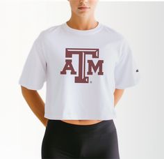 Elevate your Aggie game day attire with our Women's Texas A&M Logo Crop Top, a timeless piece that exudes pride and tradition. Crafted from premium 100% cotton, this tee ensures superior comfort during those intense moments cheering on the Aggies at Reed Arena or exploring the scenic beauty of Aggieland. Featuring the iconic Texas A&M logo front and center, this crop top is a true testament to your Aggie spirit. Whether you're attending class or hitting up Northgate for post-game celebrations, t Cotton Activewear With Graphic Print For Sports Events, White Tops With University Logo For Game Day, White Fan Apparel Tops With University Logo, White Tops With University Logo For Sports Season, Team Spirit Cotton Activewear For Sports, Athleisure Cotton Top With Team Logo, Sporty Tan Cotton Tops, White Athleisure Tops For Game Day, University Logo Cotton Short Sleeve Top