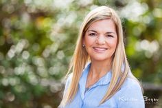 a woman with blonde hair and blue shirt posing for a photo in front of trees