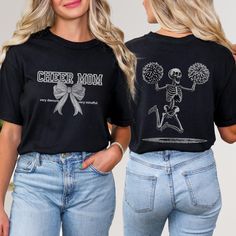 Get ready to cheer in style with this unique Front and Back Comfort Colors Shirt! The front features the words Cheer Mom in a collegiate font, adorned with a charming bow and the playful phrases very demure and very mindful on each side. But wait, the fun doesn't stop there - turn to the back of the shirt to find a large skeleton with pom-poms jumping for joy! This Cheer Mom Skeleton Comfort Colors Shirt is the perfect blend of funny and spooky, making it a must-have for any cheerleading mom. Wh Black Graphic Print Top For Cheerleading, Halloween Graphic Print Fan Apparel Tops, Halloween Skull Print Top For Fan Merchandise, Black Short Sleeve Tops For Cheerleading, Black Top With Letter Print For Cheerleading, Black Crew Neck T-shirt For Cheerleading, Graphic Cotton Tee For Cheerleading, Cotton Graphic Tee For Cheerleading, Custom Print Cotton Tops For Cheerleading