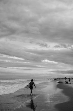 black and white photograph of people walking on the beach with surfboards in their hands